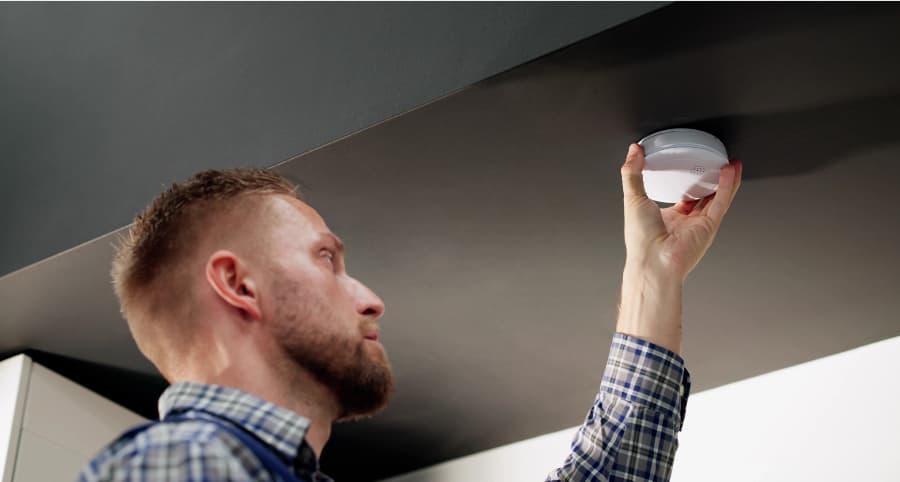 Man placing a smoke detector on ceiling of home